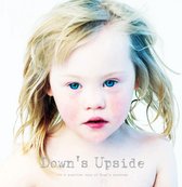 Een blond meisje met blauwe ogen en rosse wangen kijkt naar de camera. Tekst: Down's Upside, a positive view of Down's syndrome.