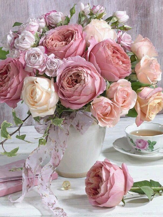 Bouquet de roses roses et crème dans un vase avec un ruban fleuri, à côté d'une tasse de thé.