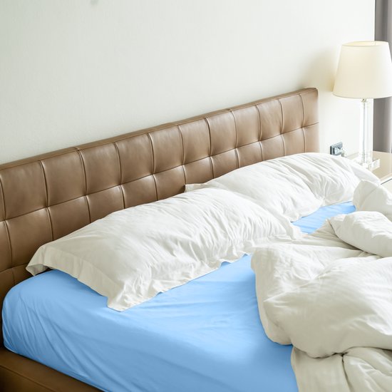 Blauw hoeslaken op een tweepersoonsbed met bruin hoofdbord en witte kussens.