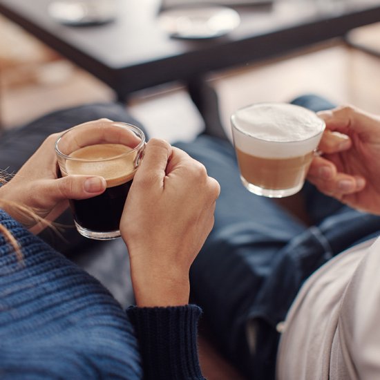 Twee handen houden een glas espresso en een glas koffie met melkschuim.
