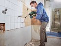 Man met masker verwijdert tegels met groene Bosch boorhamer.