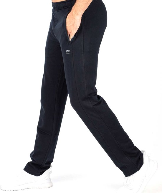 Man in zwarte joggingbroek met steekzakken, witte sneakers en 'SJS' logo op de zijkant.