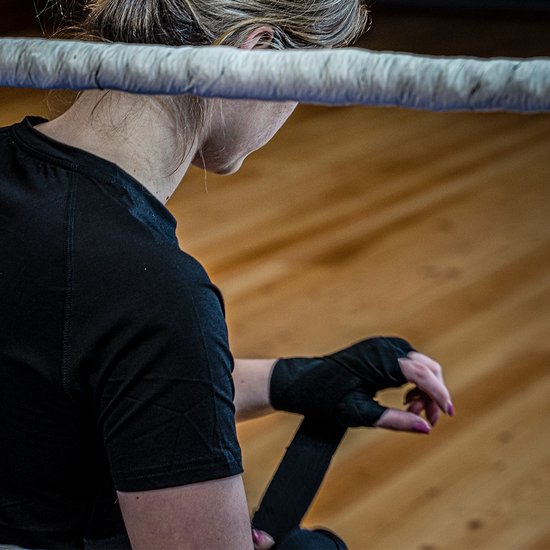 Een vrouw met zwarte bokshandschoenen, die haar rechterhand met zwarte bandages wikkelt.