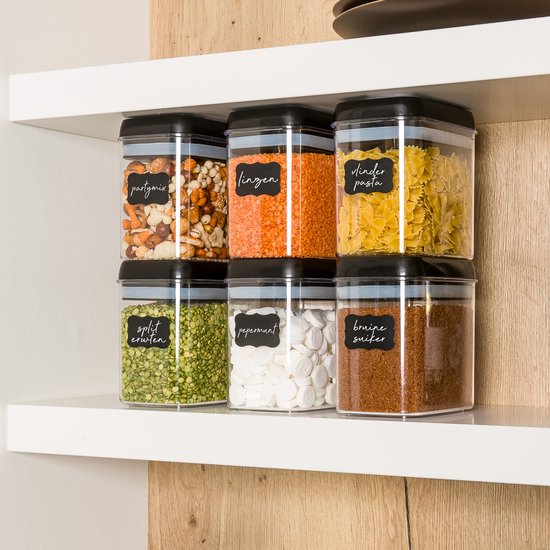 Six pots de stockage transparents empilés avec couvercles noirs, remplis de mélange apéritif, lentilles, pâtes dinder, pois cassés, menthes et sucre brun.