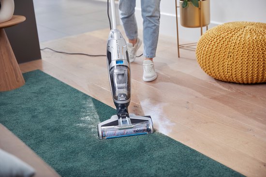 Onderkant van de Bissell Crosswave C3 Select steelstofzuiger die over een groen tapijt en houten vloer gaat.