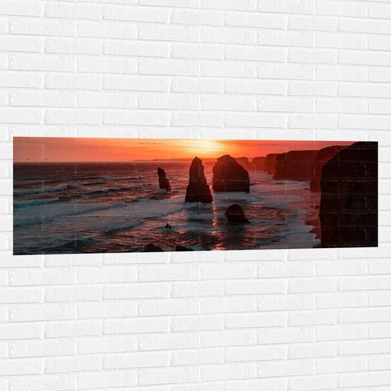 WallClassics - Muursticker - Rotsen in de Zee met Zonsondergang - 150x50 cm Foto op Muursticker