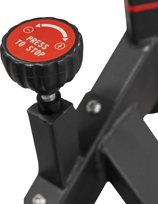 De rode weerstandsknop op de spinfiets is gelabeld met "PRESS TO STOP" en pijlen.