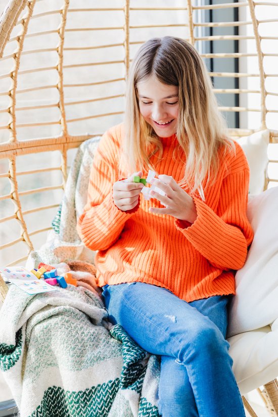 Een meisje in een oranje trui speelt met de SmartGames Puzzler in een schommelstoel.