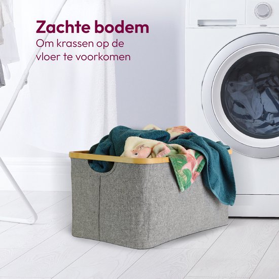 Grijze wasmand met bamboe rand gevuld met handdoeken naast wasmachine.