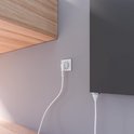 Fiche blanche avec câble branchée sur une prise murale à côté d'un radiateur anthracite.