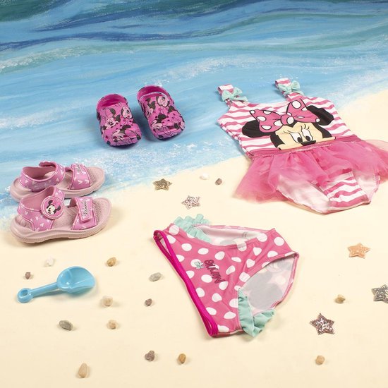 Roze Minnie Mouse badpak met strikjes, bijpassend bikinibroekje, sandalen en slippers op een strandachtergrond.