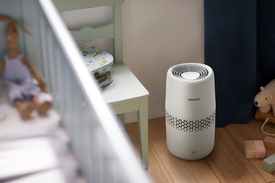 Humidificateur d'air Philips blanc sur un plancher en bois dans une chambre d'enfant, à côté de jouets.