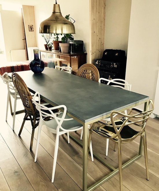 Grijze betonnen eettafel met goudkleurig metalen frame, omringd door diverse stoelen.