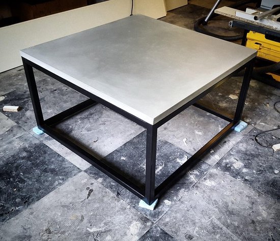 Vierkante betonnen tafel met zwart metalen frame, staand op blauwe beschermstukken.