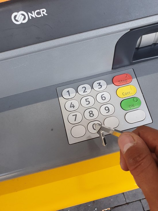 Zilverkleurige haaksleutel wordt gebruikt om de cijfertoetsen van een geldautomaat aan te raken.