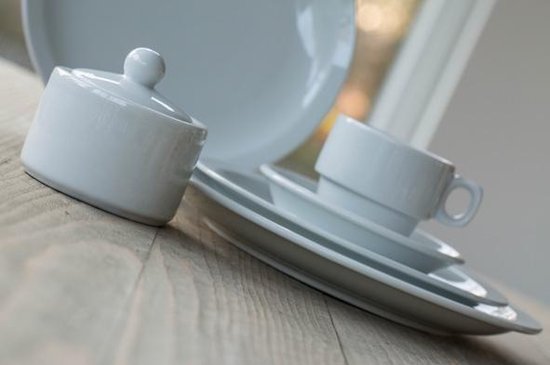 Witte suikerpot met deksel en een stapel witte borden en kopje.
