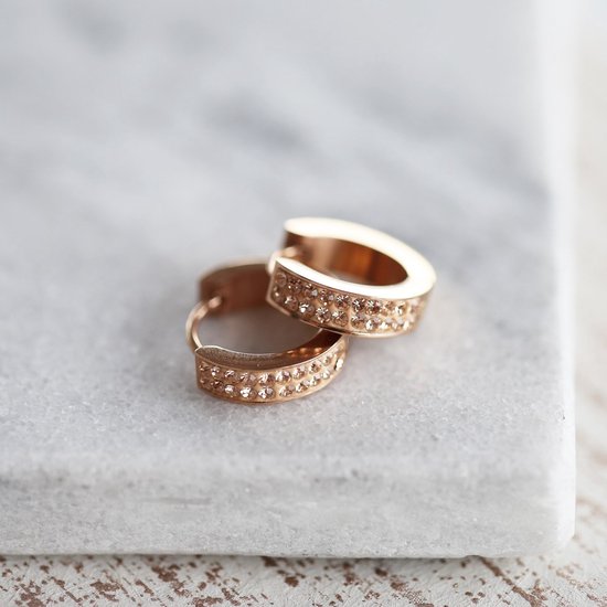 Twee rosekleurige oorbellen met perzikstenen op een marmeren ondergrond.