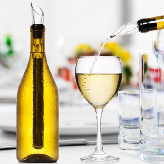 Witte wijn wordt uit een glazen fles met een zilverkleurige en transparante wijnkoeler geschonken in een glas. Op de achtergrond staan meer glazen.