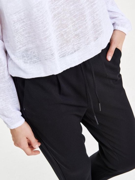 Detail van zwarte broek met ceintuur met tunnelkoord, gedragen met een witte longsleeve.