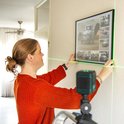 Vrouw met oranje trui hangt lijst op met behulp van groene laserlijnen.