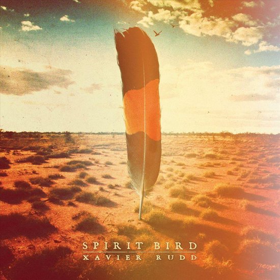 Grote veer met bruine, oranje en zwarte strepen in een dorre woestijnlandschap onder een zonnige hemel. Tekst: SPIRIT BIRD XAVIER RUDD.