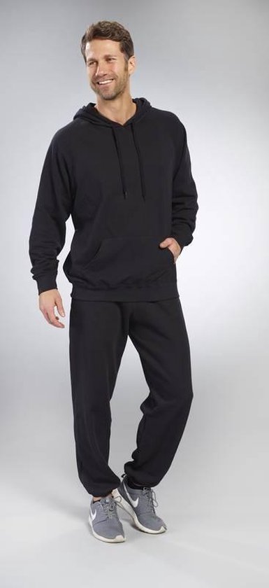 Man draagt een zwarte hoodie met capuchon, buidelzak en zwarte joggingbroek. Handen in de zakken.