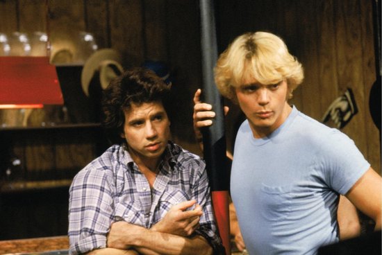 Twee mannen, één met een geruite blouse en één met een blauw shirt, staan in een bar.