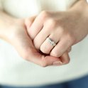 Prise détaillée d'une bague argentée sertie de zircons sur un doigt.