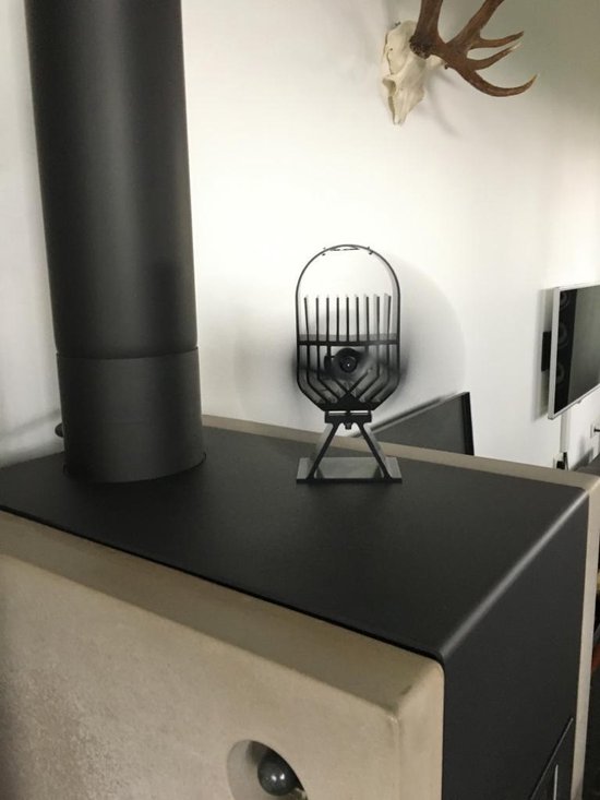 Zwarte kachelventilator op de bovenkant van een moderne grijze houtkachel, naast een zwarte schoorsteen.