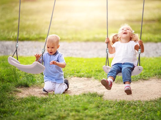 Un petit garçon à genoux et une petite fille souriante sur une balançoire, jouant à l'extérieur.