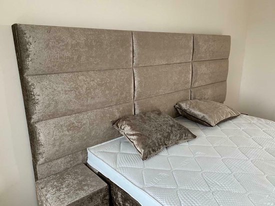 Grijze boxspring met een hoog hoofdbord en een matras, met twee kussens.