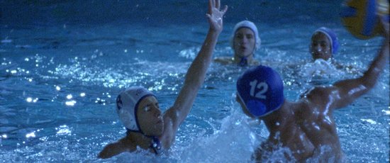 Een waterpolowedstrijd met spelers in witte en blauwe caps. Speler 12 draagt een blauwe cap.