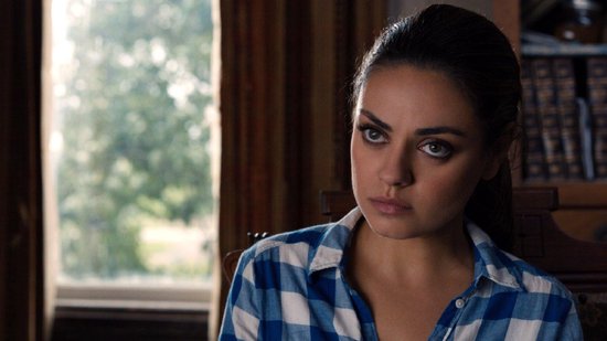 Mila Kunis in een blauw-wit geruit hemd kijkt geconcentreerd de camera in.