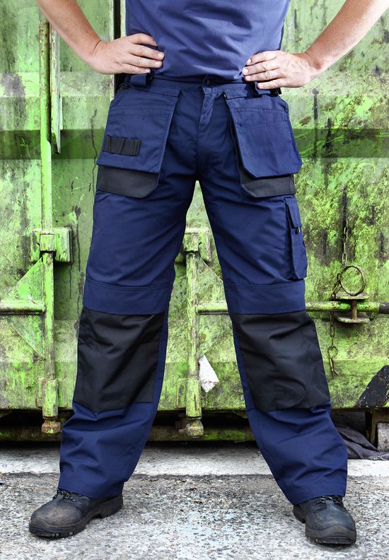 Marineblauwe werkbroek met zwarte accenten op de zakken en knieën, gedragen door een model.