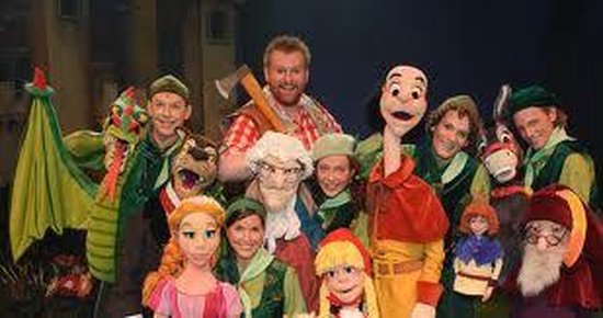 Een groep acteurs en poppen uit 'Sprookjesboom', waaronder een draak, een wolf en kabouters, poseren samen.