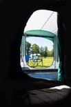 Gezien vanuit de tent, buiten staan 2 blauwe stoelen en een tafel op een grasveld.
