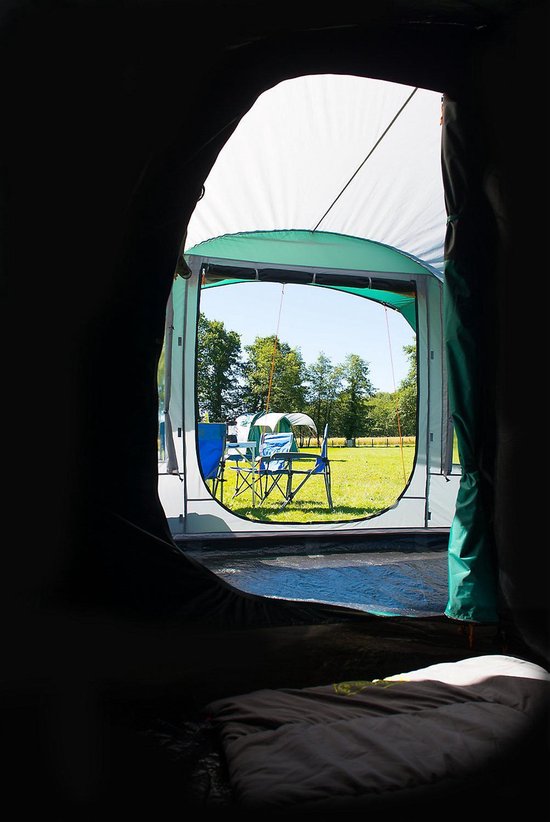 Gezien vanuit de tent, buiten staan 2 blauwe stoelen en een tafel op een grasveld.