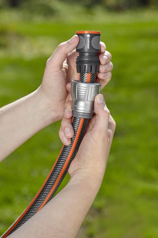 Handen bevestigen een grijze en zwarte Gardena slangkoppeling met oranje accenten aan een tuinslang.