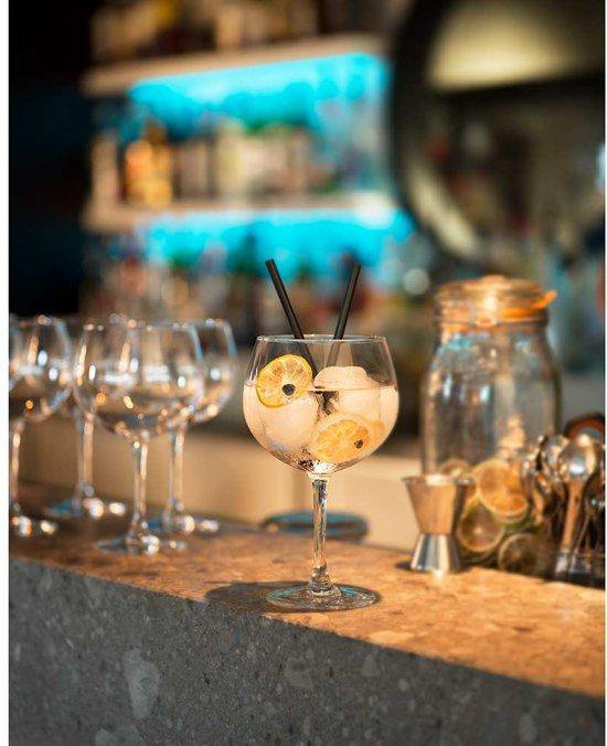 Een cocktailglas gevuld met ijs, partjes citroen en twee zwarte rietjes.