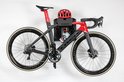 Zwarte en rode racefiets met rode helm en bidon op een Stasdock muurbeugel.