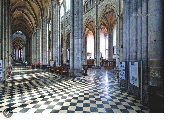 Interieur van een kathedraal met een zwart-witte tegelvloer, hoge zuilen en glas-in-loodramen.