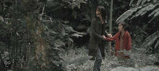 Een vrouw in een groen jasje en een meisje in een rood jasje lopen hand in hand in een bosrijke omgeving.