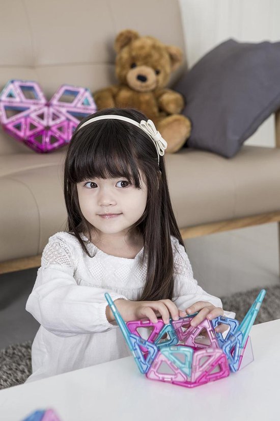 Meisje met lang zwart haar en witte kanten top speelt met roze en blauwe Magformers.