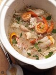 Zeer dichtbij van vis en garnalen in een romige, kruidige bouillon in een witte slowcooker.