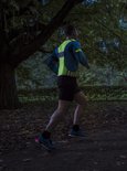 Man joggend in het donker met een fluoriserend geel en blauw sportshirt met reflecterende details.