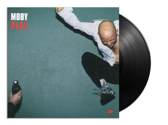 Moby Play vinyl albumhoes met Moby die in de lucht springt, naast een zwarte vinylplaat.