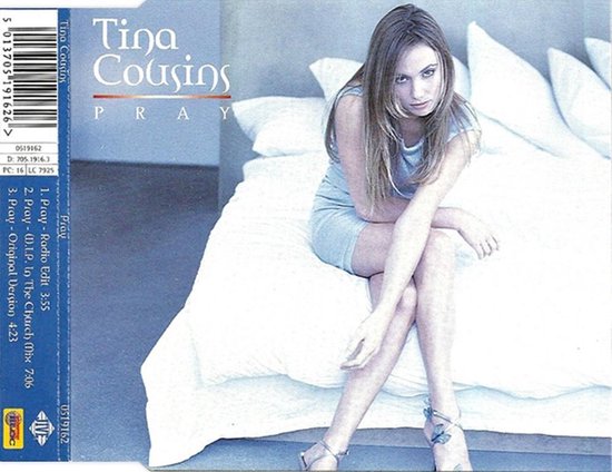 Tina Cousins zit op een wit bed, gekleed in een blauw jurkje en hakken. "Tina Cousins PRAY" staat bovenaan.