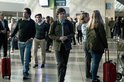 Mensen lopen door een drukke luchthavenhal met bagage, een jonge man op de voorgrond.