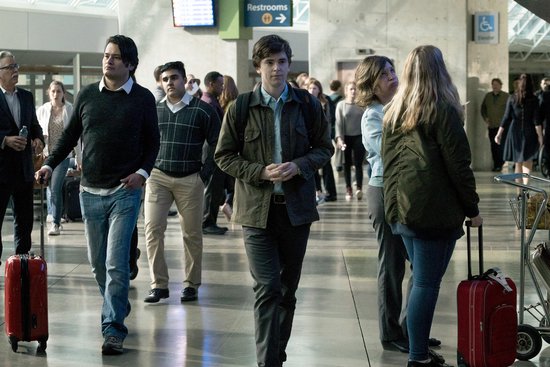 Mensen lopen door een drukke luchthavenhal met bagage, een jonge man op de voorgrond.
