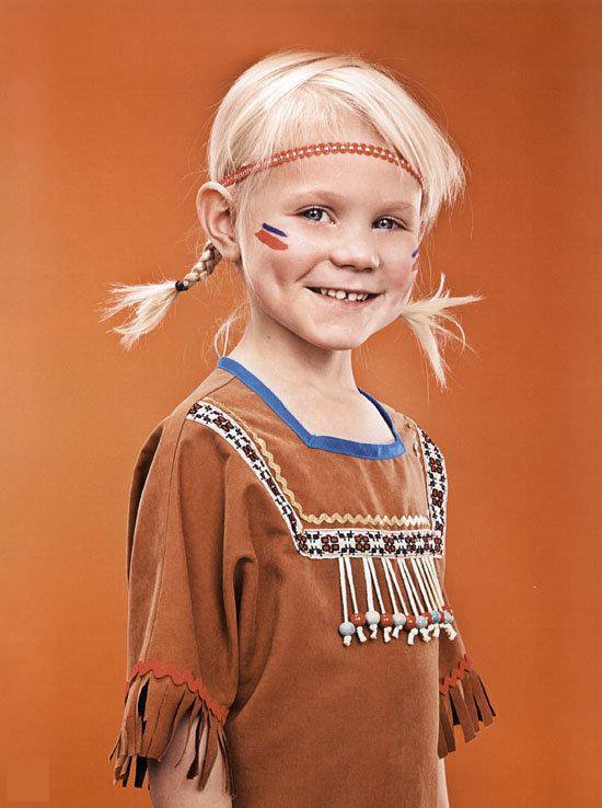 Een lachend meisje met blonde vlechtjes, rode hoofdband en gezichtsverf in indiaanse stijl.
